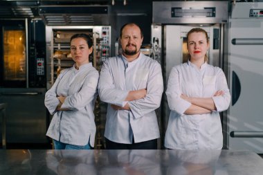 Pişirmeye başlamadan önce profesyonel bir mutfakta gülümseyen profesyonel fırıncılardan oluşan bir ekip.