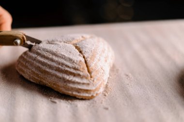 Kadın fırıncı, fırın yapımı hamur işlerini kapatmadan önce, profesyonel bir fırın bıçağıyla çiğ ekmek rulolarında desenler kesiyor.