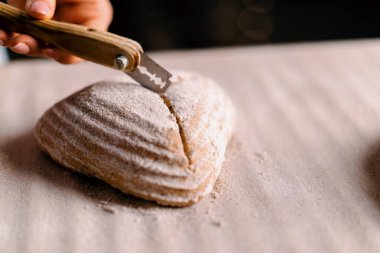 Kadın fırıncı, fırın yapımı hamur işlerini kapatmadan önce, profesyonel bir fırın bıçağıyla çiğ ekmek rulolarında desenler kesiyor.