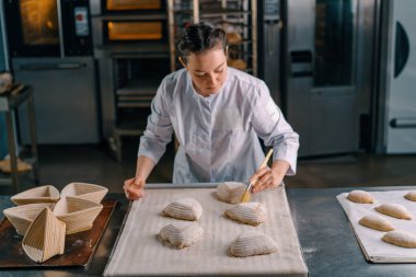 Konsantre güzel kadın fırıncı fırın hamur işleri pişirmeden önce çiğ ekmeğe yumurta sürer.