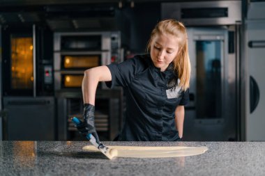 Çikolata üretimini yumuşatan pasta şefi, erimiş çikolatayı hamur işi masasında metal bir spatulayla karıştırıyor.
