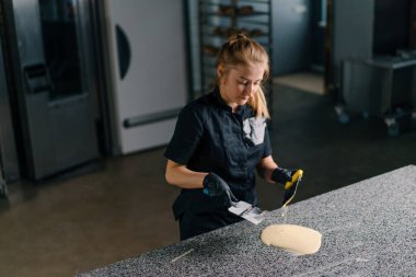 Çikolata üretimini yumuşatan pasta şefi, erimiş çikolatayı hamur işi masasında metal bir spatulayla karıştırıyor.