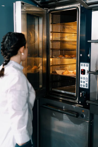 魅力的なベイカーは準備ができているパンとクロワッサンプロのオーブンベーカリー生産新鮮な焼き菓子を取ります — ストック写真