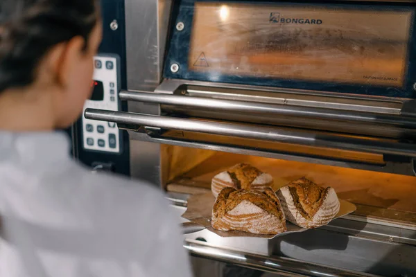 女面包师从烤箱中取出刚烤好的新鲜面包 放在烹调行业厨房的架子上 — 图库照片