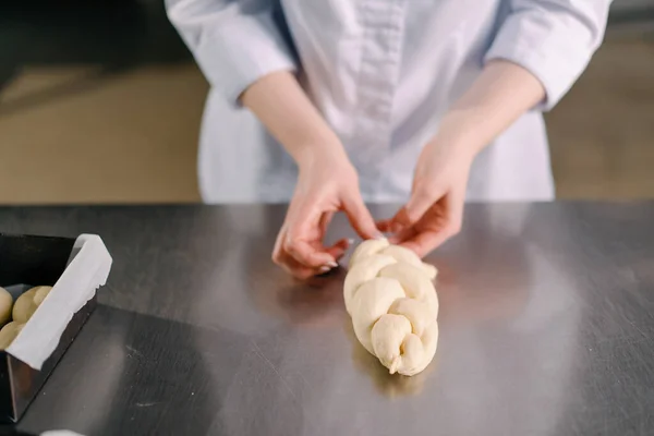 面包师在厨房专业的厨房烘焙糕点生产中用生面团做成了一个辫子 — 图库照片