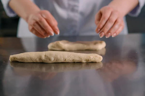 面包师在厨房专业的厨房烘焙糕点生产中用生面团做成了一个辫子 — 图库照片