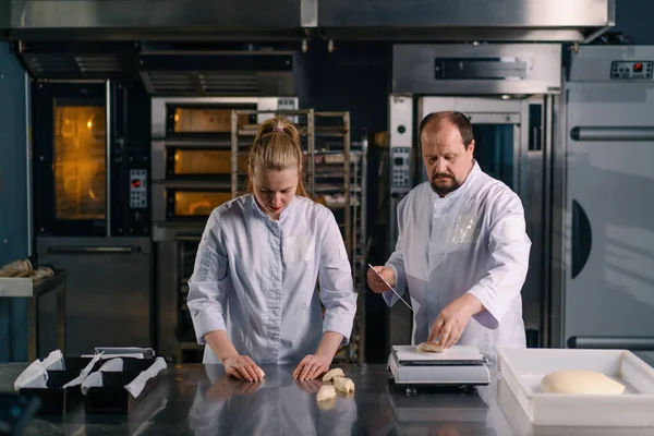 İki fırıncı hamur işini pişirmeden önce şekillendirir, keser ve profesyonel pasta imalatına sunar.