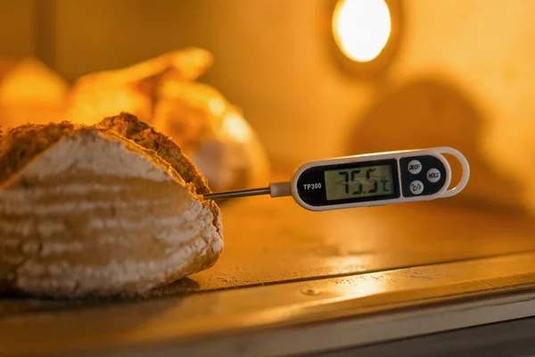 面包师用温度计烘焙生产的糕点测量烤箱中新鲜烘焙面包的温度 — 图库照片