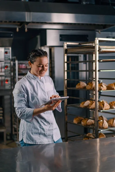 Kvinnlig Bagare Uniform Nära Hyllorna Med Nybakat Bröd Håller Tablett — Stockfoto