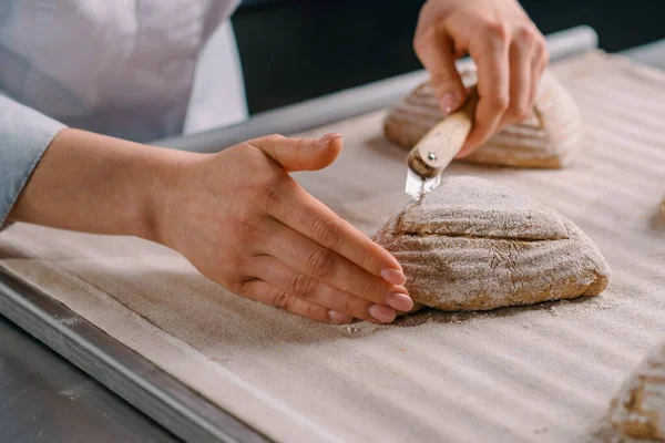 女面包师在烘焙面包店生产糕点前 用专业面包师的刀切生面包卷上的花纹 — 图库照片