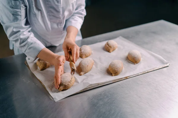 女面包师在烘焙面包店生产糕点前 用专业面包师的刀切生面包卷上的花纹 — 图库照片