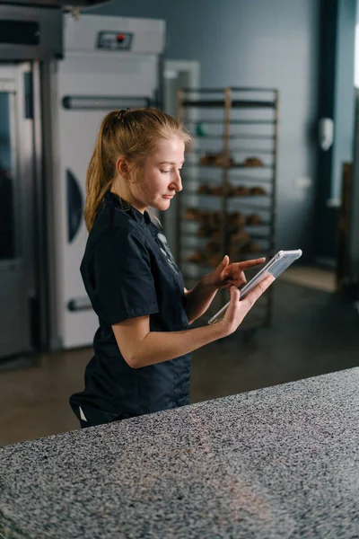Profesionální Cukrář Uniformě Tabletem Ruce Kontroluje Úkoly Před Zahájením Práce — Stock fotografie