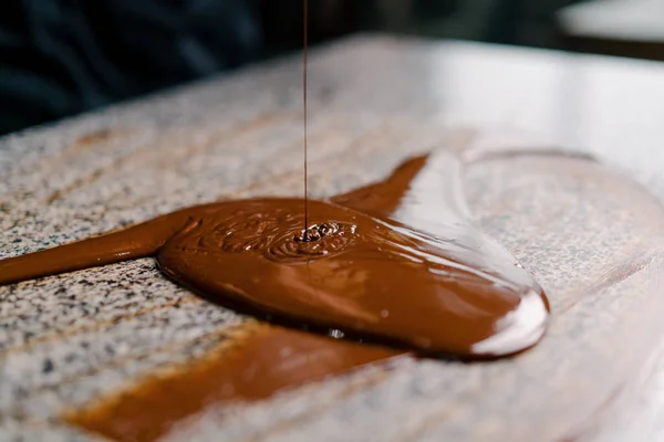 Tempering chocolate production of chocolate candies - pastry chef mixes melted chocolate with a metal spatula on a table in pastry shop