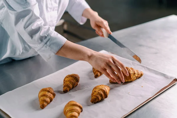 漂亮的女面包师用小刀切碎刚烤好的热脆香味羊角面包 并检查面团的生产情况 — 图库照片