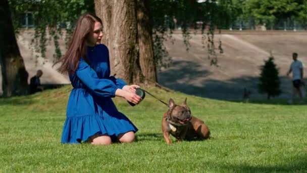 公園でフランスのブルドッグと散歩している美しい女の子は リーシュにかわいい小さな犬と遊びます — ストック動画