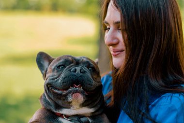 Genç sahibinin kucağında küçük sevimli bir Fransız bulldog var. Doğadaki bir hayvan portresi gibi gülümsüyor.