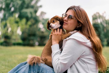Parkta gezintiye çıkmış küçük, sevimli bir köpek. Kız sarılıyor ve evcil hayvan arkadaşına sarılıyor.