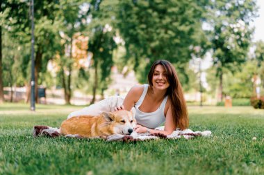 Doğada dinlenen genç ve güzel bir kız parkta bir çarşafa uzanmış küçük Corgi köpek hayvanlarıyla oynuyor.