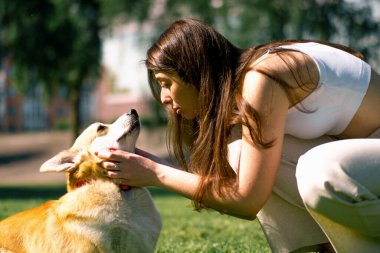 Genç bir kızın portresi ve şirin bir Corgi köpeği. Sahibi parkta yürürken köpeği burnundan öper.