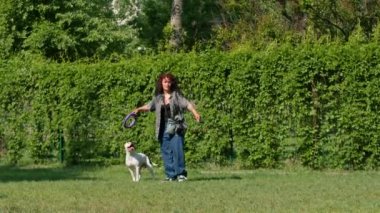 Genç bir kız parkta büyük bir pitbull cinsinin beyaz köpeğiyle oynuyor. Köpek onun peşinden koşuyor ve oyuncağını dişleriyle çekiyor.