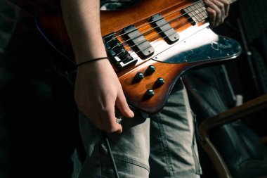 Kayıt stüdyosunda elektro gitarlı bir rock sanatçısı, telle bağlanan bir müzik aletini elinde tutuyor.