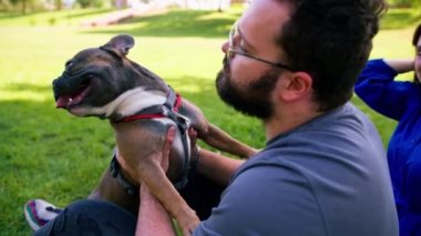 Evli bir çift doğada dinleniyor. Parkta bir çarşafta yatıyor. Fransız buldog cinsinden küçük bir köpekle oynuyor.