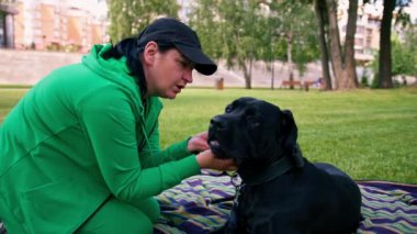 Büyük siyah bir köpek kamışı Corso 'su olan kadın antrenör parkta çim çalıyordu.