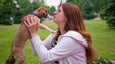 Parkta gezintiye çıkmış küçük sevimli köpeği olan kız doğadaki evcil hayvanın burnunu öpüyor.