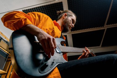 Stüdyoda elektro gitarlı bir rock müzisyeni kendi müzik enstrümanı tellerini çalıyor.