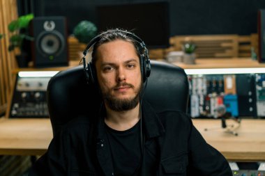 Profesyonel müzik stüdyosunda kulaklık takan genç ciddi ses mühendisinin portresi.