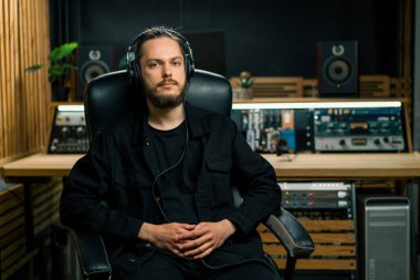 Profesyonel müzik stüdyosunda kulaklık takan genç ciddi ses mühendisinin portresi.