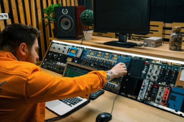 Genç ses mühendisi müzik stüdyosunda monitörler ve ekolayzır ile çalışıyor. Şarkıları karıştırıyor ve ana parçaların ses kaydını yapıyor.