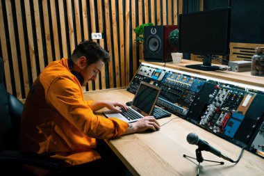 Genç ses mühendisi müzik stüdyosunda çalışıyor. Monitörler ve ekolayzır ile şarkı kaydeden mikrofon masalarını karıştırıyor ve ustalaştırıyor.