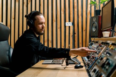 Müzik stüdyosunda çalışan kulaklıklı genç bir ses mühendisi. Monitörleri ve ana parçaları karıştıran bir ekolayzır.