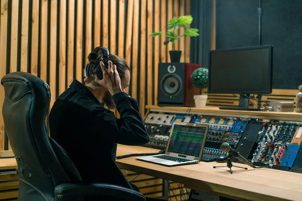 年轻的音响工程师戴上耳机 在专业的音乐工作室里工作 带着监视器和一个混合着主控曲目的均衡器 — 图库照片
