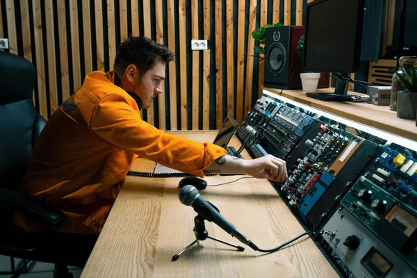 Genç ses mühendisi müzik stüdyosunda çalışıyor. Monitörler ve ekolayzır ile şarkı kaydeden mikrofon masalarını karıştırıyor ve ustalaştırıyor.