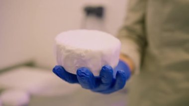 Elinde kağıt ambalajında organik yumuşak peynir tutan bir işçi. Yakın plan peynir üretimi.