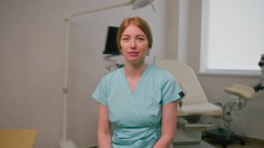 Gülümseyen doktor jinekolog, jinekoloji ofisinde, ultrason makinesinin yanında oturuyor ve hastaları bekleyen jinekoloji kürsüsünde.