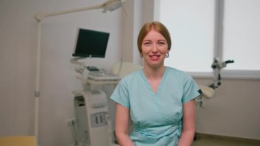 Gülümseyen doktor jinekolog, jinekoloji ofisinde, ultrason makinesinin yanında oturuyor ve hastaları bekleyen jinekoloji kürsüsünde.