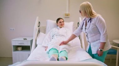 Bir doktor hastane odasında teşhisi açıkladıktan sonra bir hastanın elini tutar ve ona destek olur.