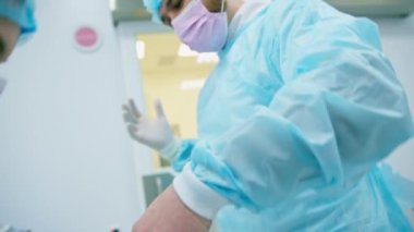 Ameliyathane hazırlama ameliyatında hemşire, cerrahın ameliyat üniforması giymeden önce steril eldiven giymesine yardım ediyor.