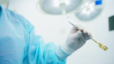 Steril eldivenli bir hemşire hastanede ameliyat sırasında cerraha makası uzatıyor.