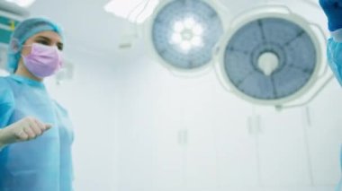 Ameliyat sonrası eldiven giyen doktorlar ameliyathanede meslektaşlarının yanında el ele tutuşuyorlar.