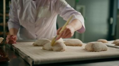 Konsantre güzel kadın fırıncı fırın hamur işleri pişirmeden önce çiğ ekmeğe yumurta sürer.