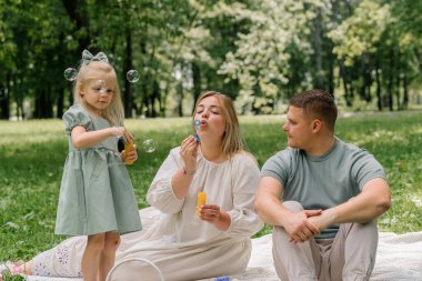 Mutlu aile parkta dinleniyor anne ve kız sabun köpüğü üflüyor eğlenceli çocukluk aile hafta sonu anneler günü