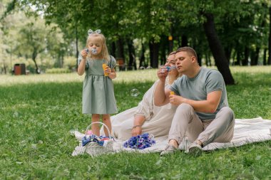 Mutlu aile parkta dinleniyor baba ve kız sabun köpüğü üflüyor eğlenceli çocukluk ailesi hafta sonu eğlencesi