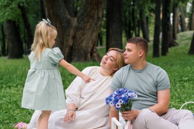 Mutlu aile parkta dinleniyor. Küçüklerin doğum gününü kutluyorlar. Bir buket çiçek çocuğa sarılıyor.