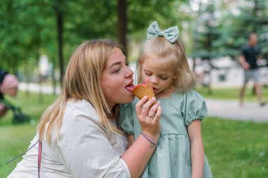 Küçük şirin kız yeşil yaz elbisesi. Annenle birlikte şehir parkında dondurma yiyor. Aile hayatı.