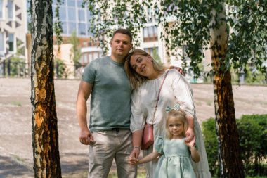 Gülümseyen genç bir ailenin portresi. Anne, baba ve küçük kız aile parkta mutlu bir çocukluk geçiriyor.