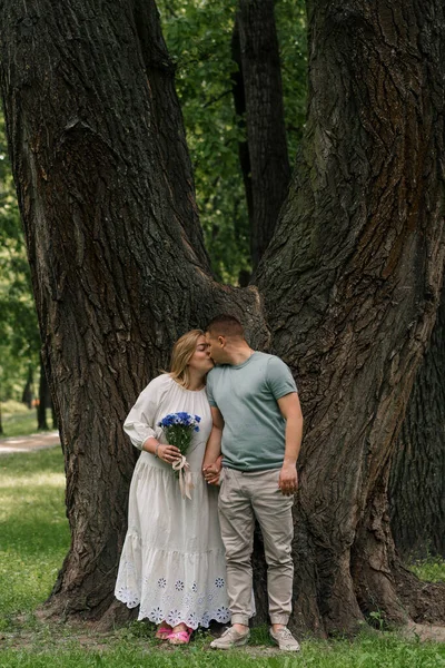 愛する夫婦の肖像画 男と公園の花を持つ妊婦 幸せな家族カップルの追加を待っている — ストック写真